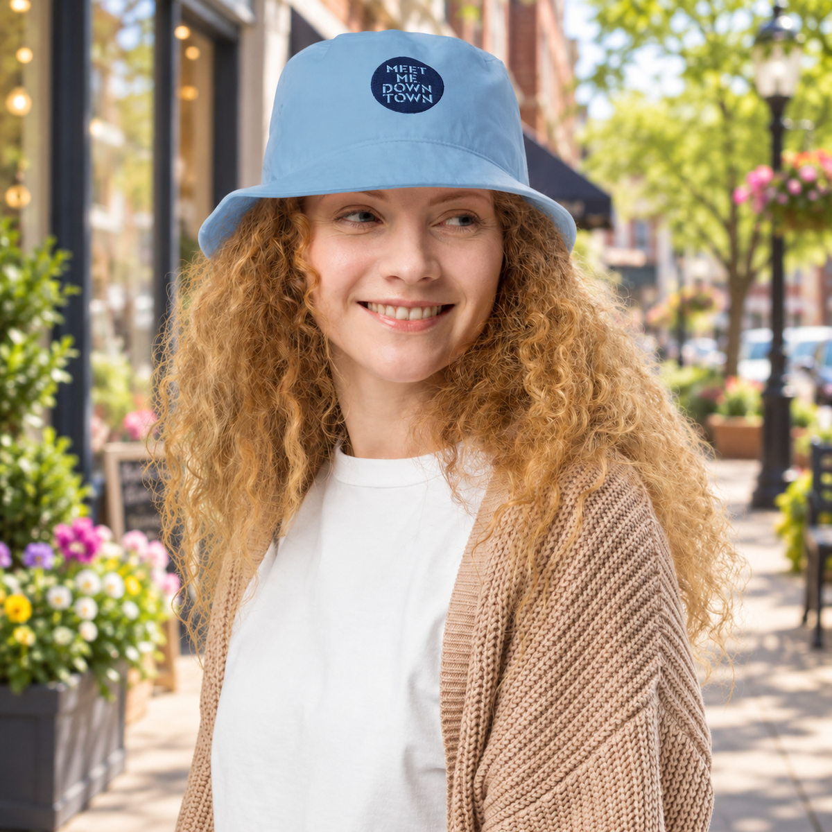 Woman wearing blue bucket hat reading "Meet me downtown" while standing on downtown street